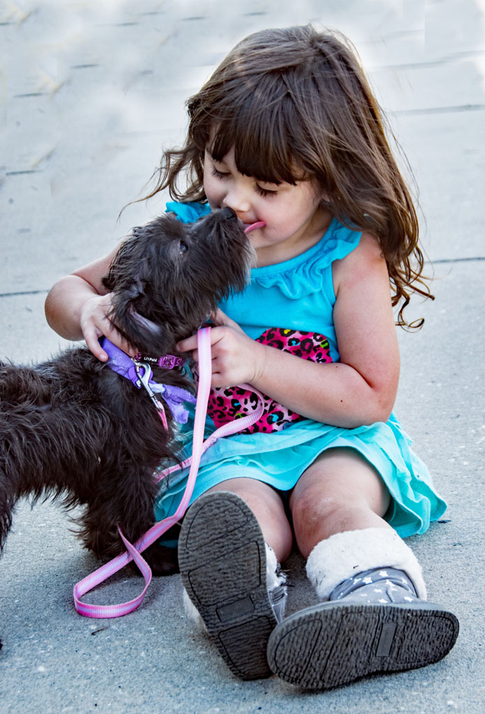 A little girl sitting on the ground with her dog.