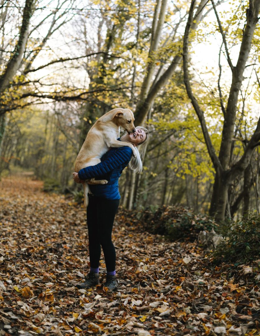 A woman holding her dog in the woods