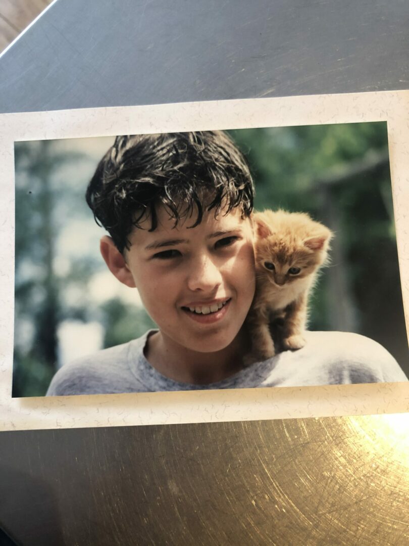 A young boy holding a cat on his shoulder.
